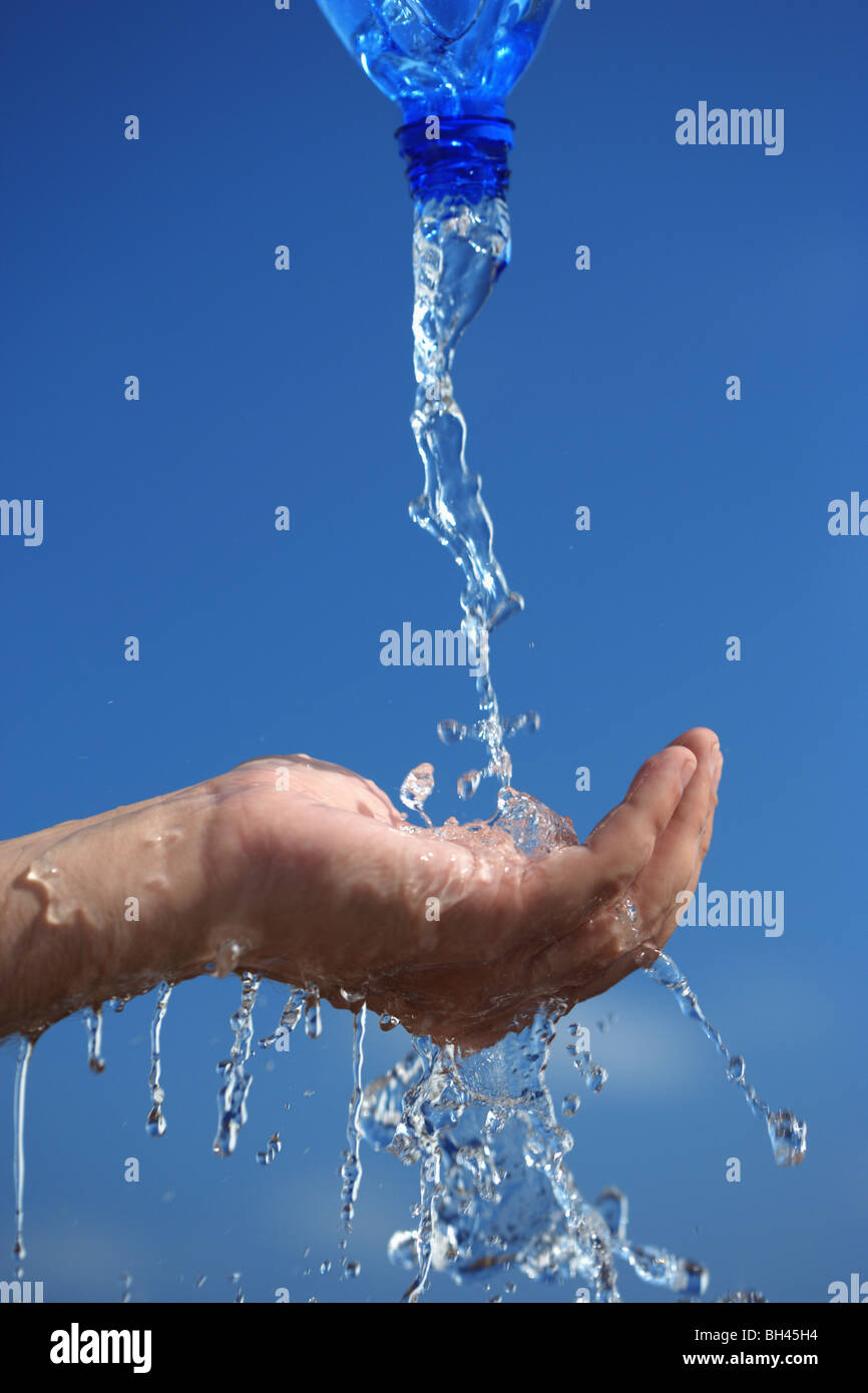 Water splashing from a bottle on to the palm of a man's hand against a blue background Stock Photo
