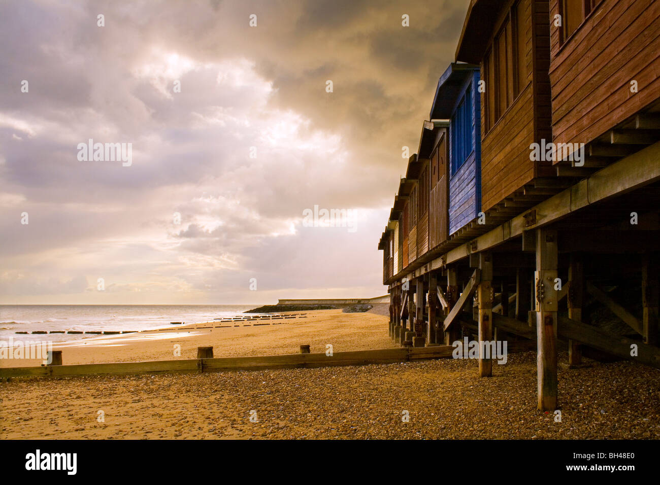 Beach huts on stilts on a sandy beach next to the sea at Frinton-on-Sea. Stock Photo