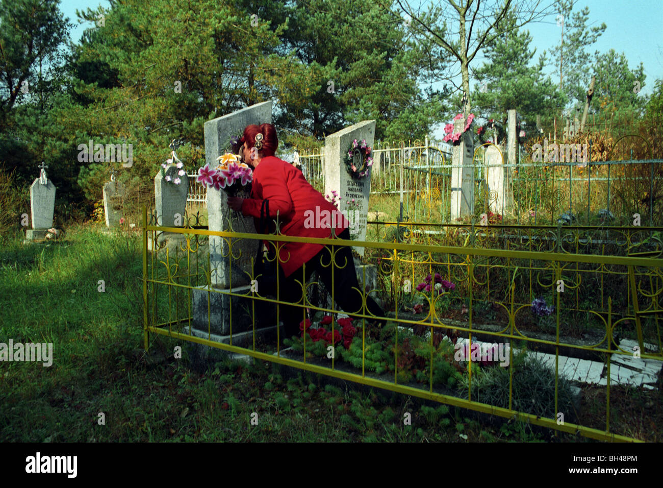 A Belarusian woman kisses a photo of her mother at her family's gravesite in a rural village. Stock Photo