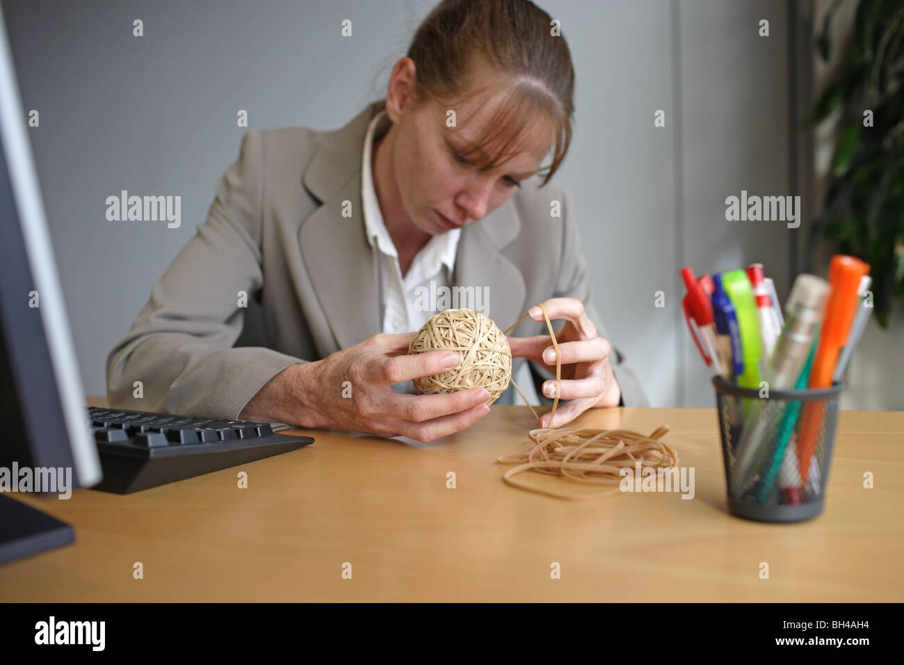 A businesswoman making a rubber band ball at an office desk with an