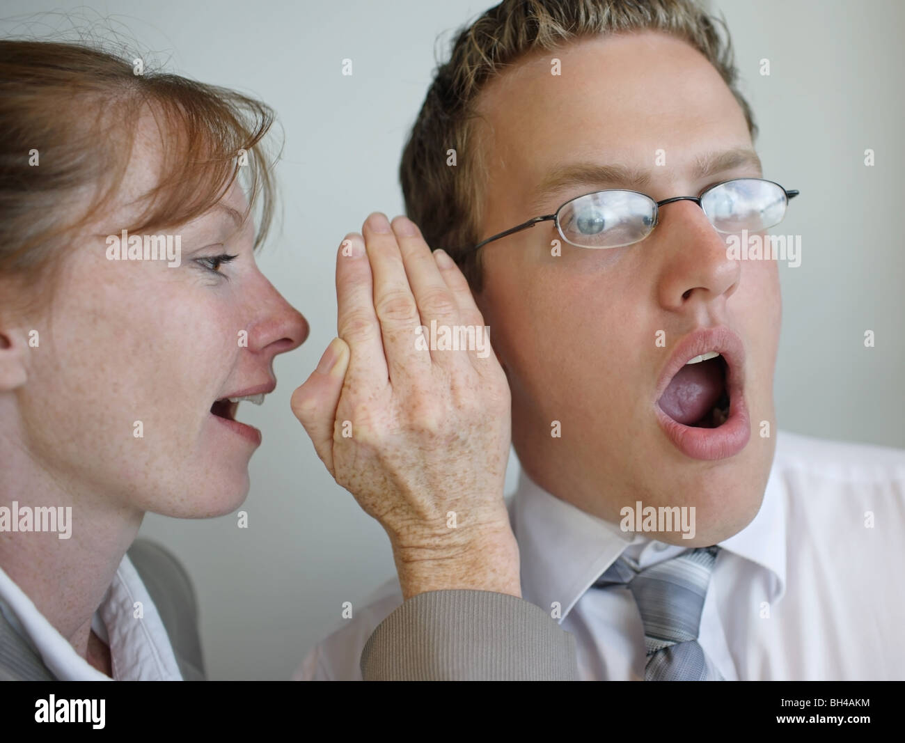 An office worker whispering in the ear of a colleague, with a shocked