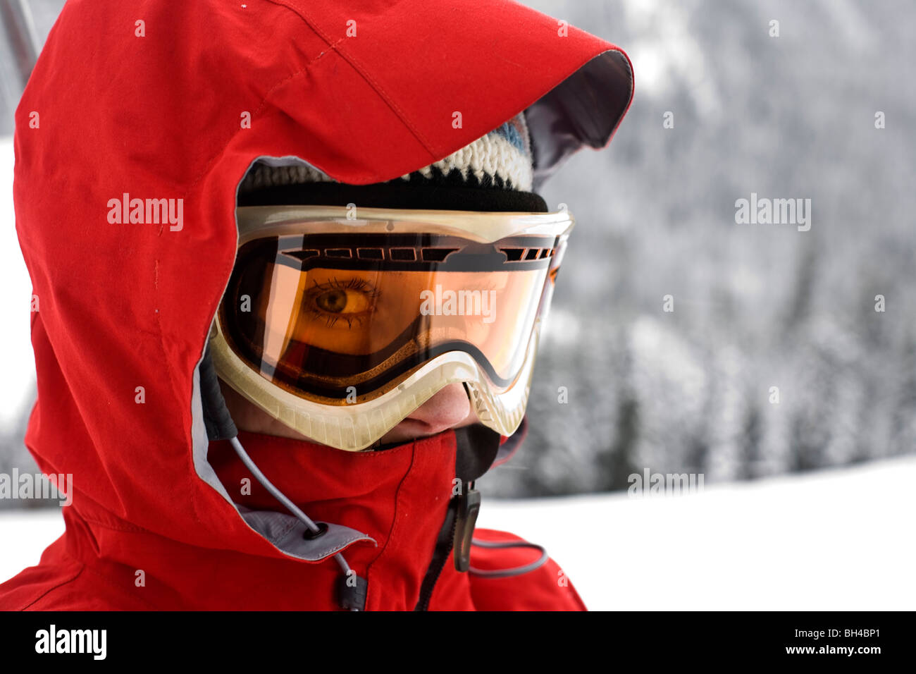 A close-up portrait of a woman wearing a red ski coat, goggles and ski cap looking directly into camera with just her nose and e Stock Photo