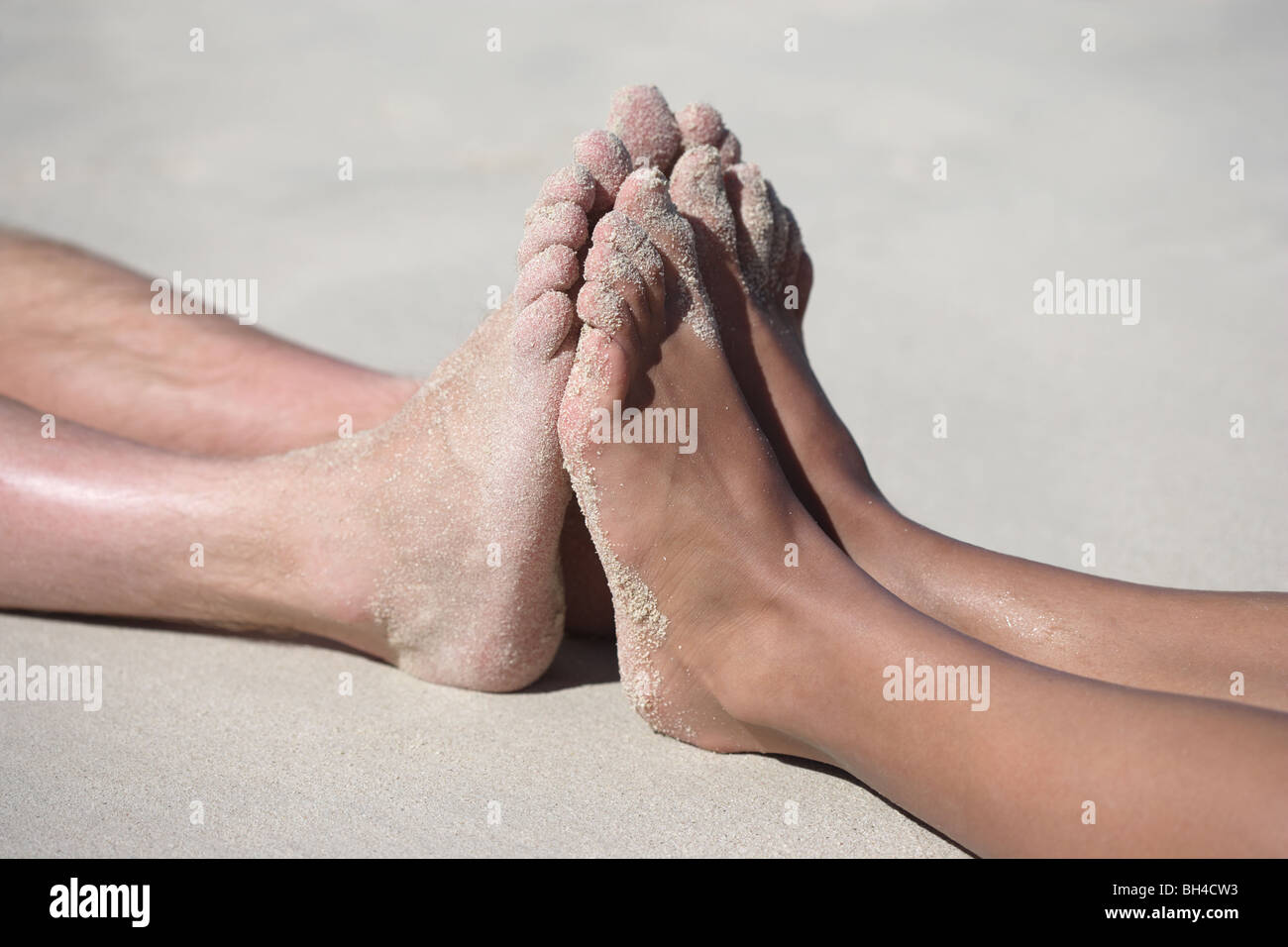 A man and a woman pressing their feet against each other lying on a sandy beach Stock Photo