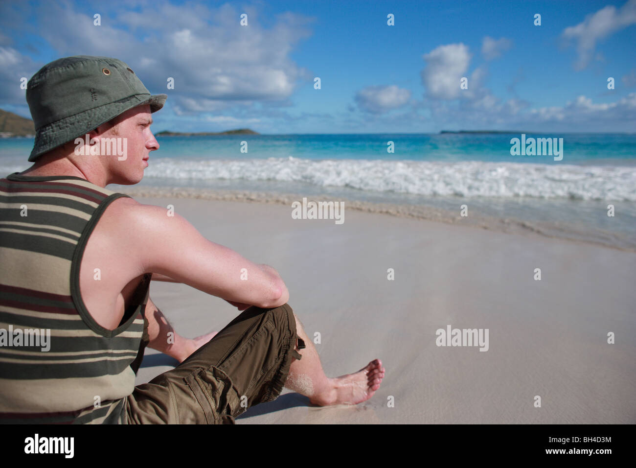 Young man sitting on a deserted tropical beach looking out towards the horizon Stock Photo