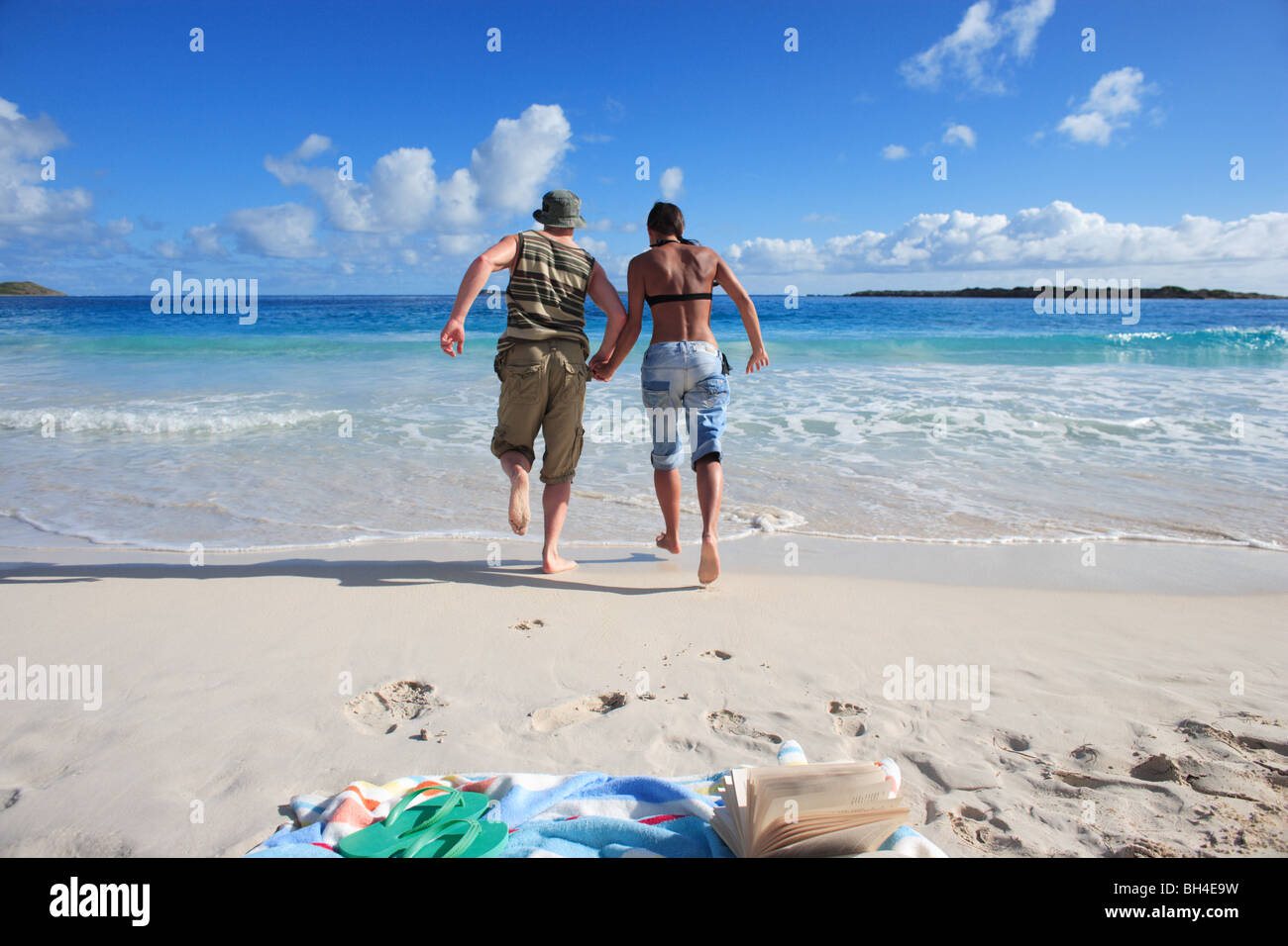 Young couple holding hands and fully clothed as they run into the sea on a deserted tropical beach Stock Photo