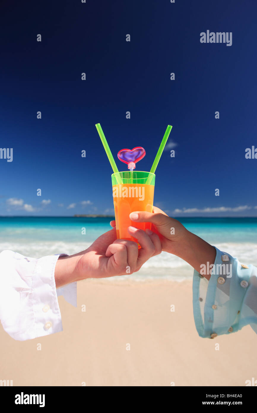 Young couple holding a single tropical cocktail on a deserted tropical beach Stock Photo