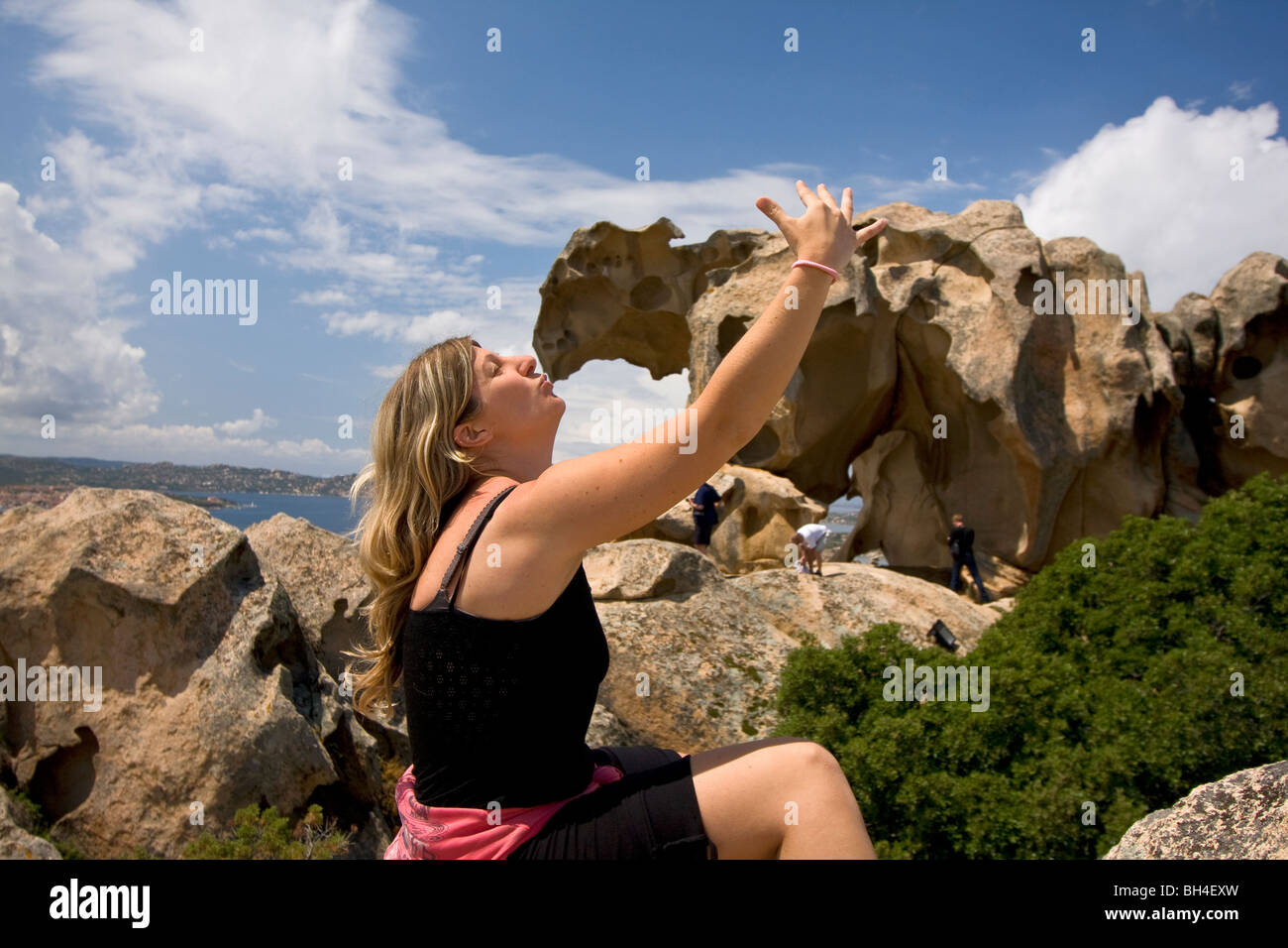 Young girl kissing the big bear stone shaped by wind and meteorological element at Capo d'Orso. Palau, Sardinia. Italy Stock Photo