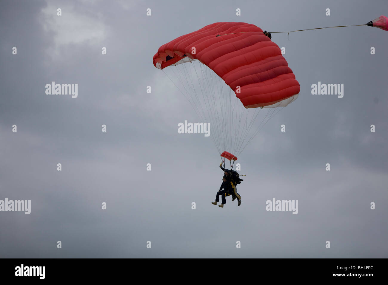 Two people in tandem parachute jump preparing for landing Stock Photo