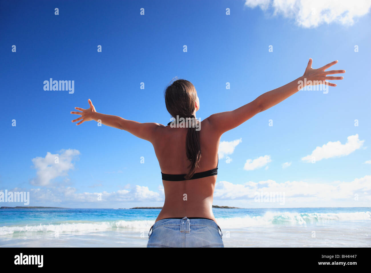 Young woman with her arms raised in celebration towards the sky on a deserted tropical beach Stock Photo