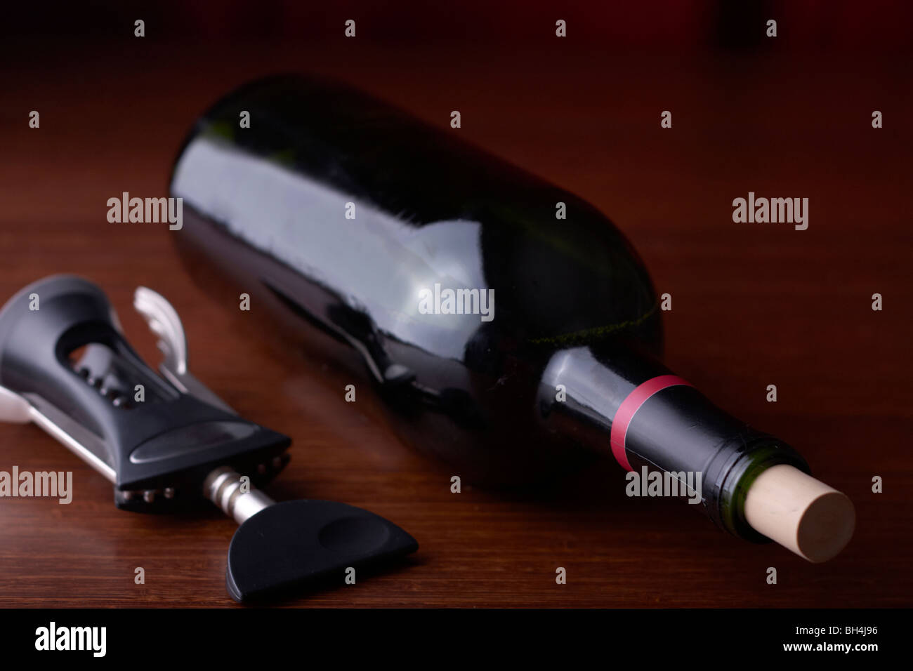 A wine bottle sits on a table with a corkscrew Stock Photo