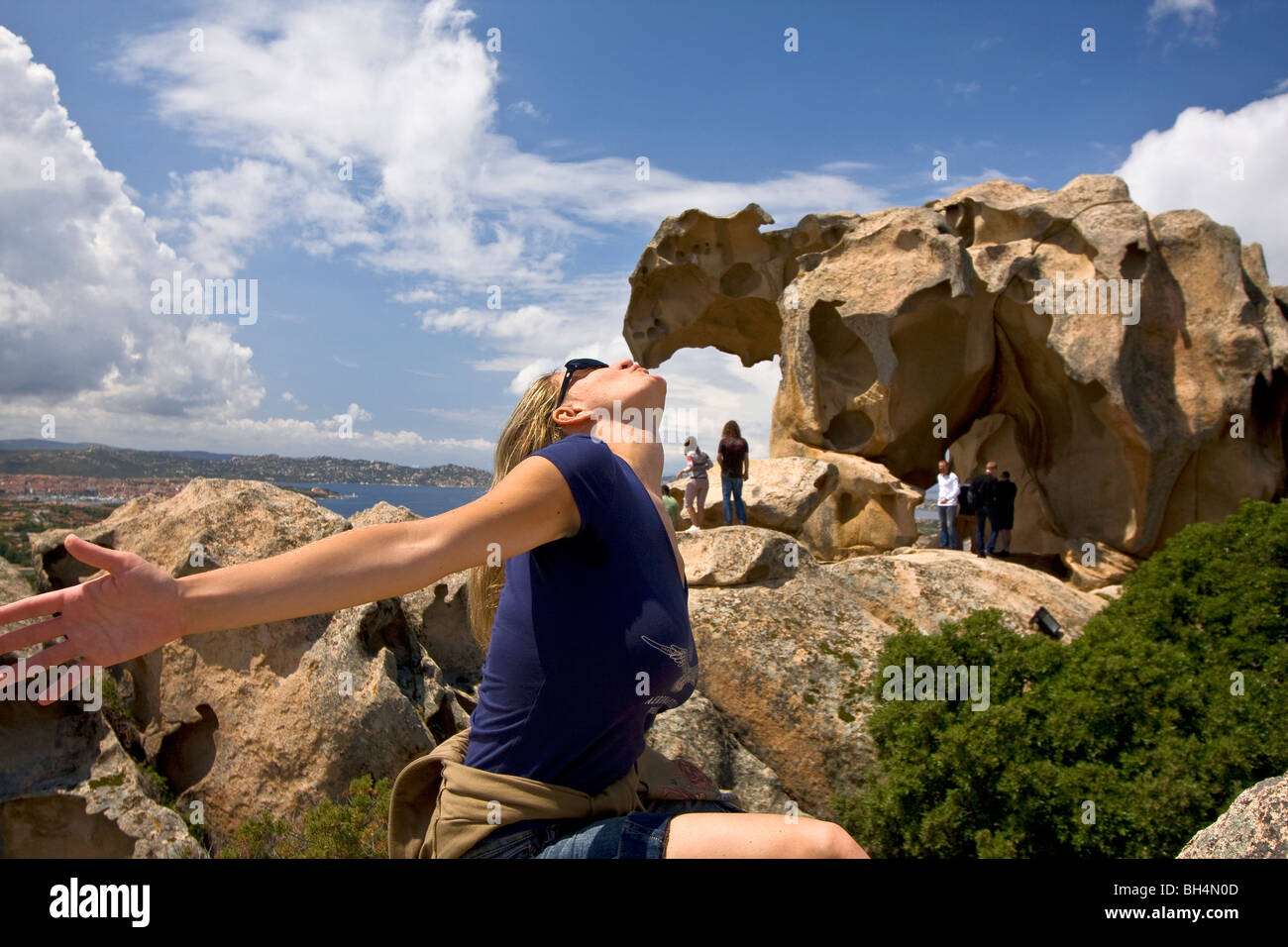 Young girl kissing the big bear stone shaped by wind and meteorological element at Capo d'Orso. Palau, Sardinia. Italy Stock Photo