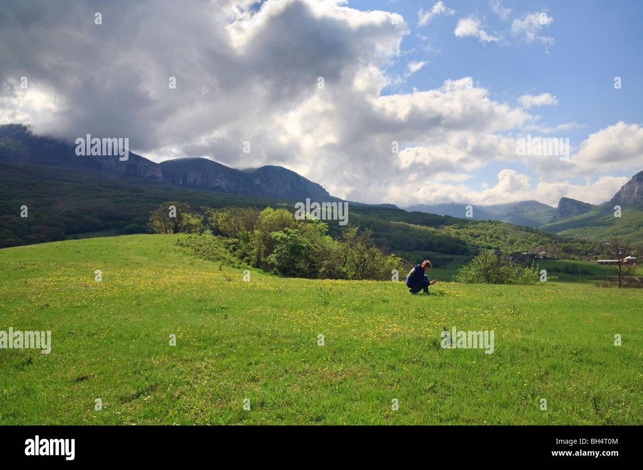 spring mountain landscape, meadow with yellow flowers and woman with camera (environs of Sokolinoe village , Crimea, Ukraine) Stock Photo
