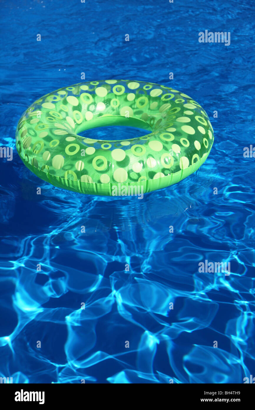 An inflatable green plastic ring swimming in a shiny blue swimming pool. Stock Photo