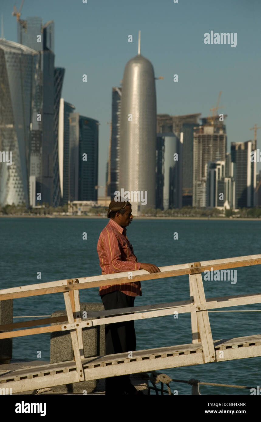 Portrait view of the Doha skyline with a man standing next to a boat gangway in the foreground Stock Photo