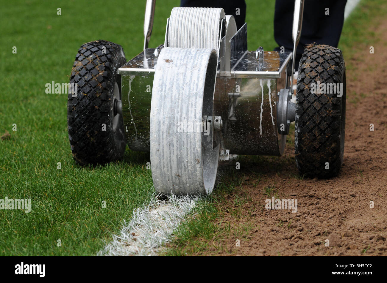 Groundsman putting a white line down a football pitch using a push
