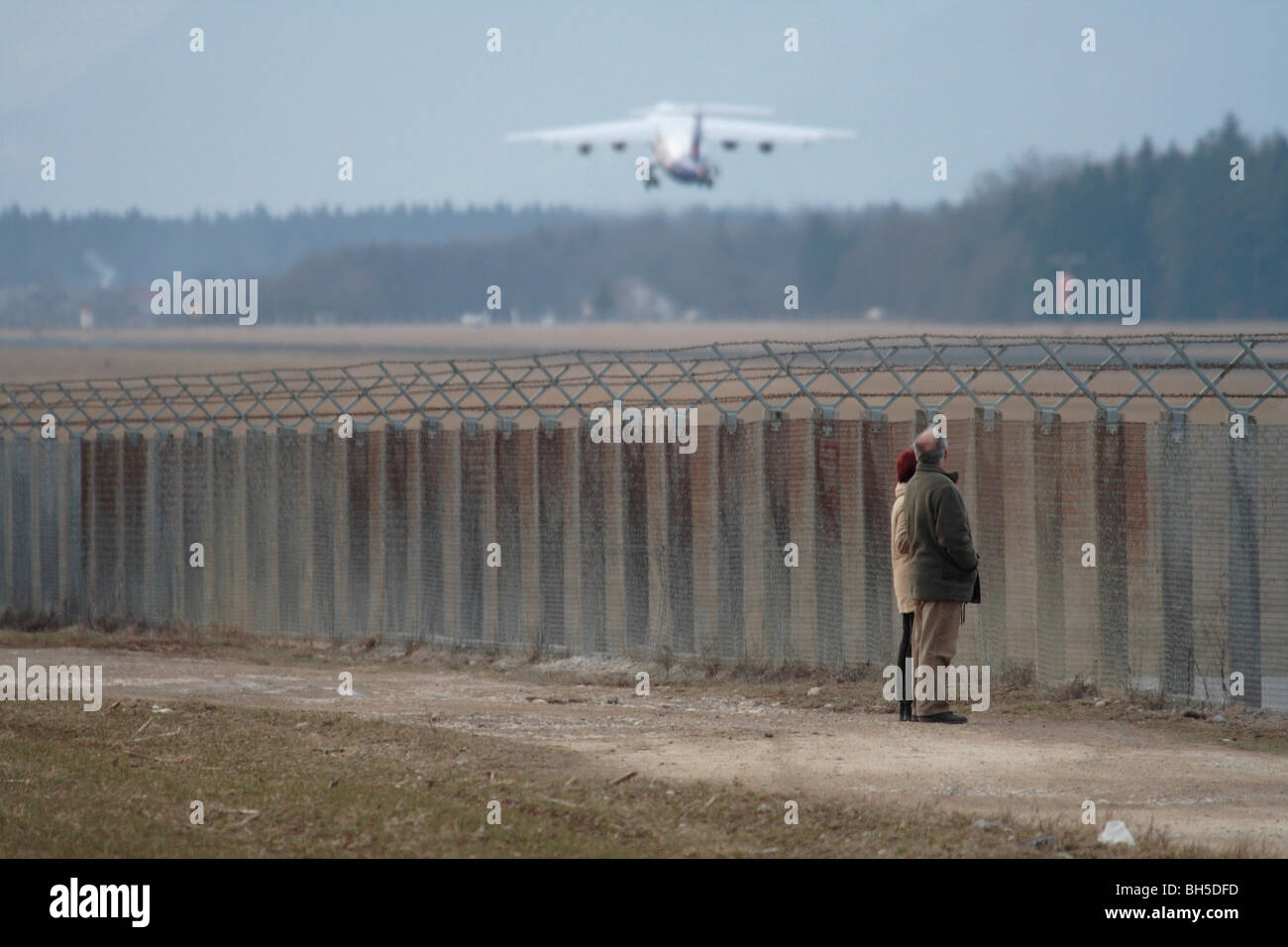 Walkers outside the perimeter fence at Ljubljana Airport watching an aircraft taking off. Air traffic and aviation. Stock Photo