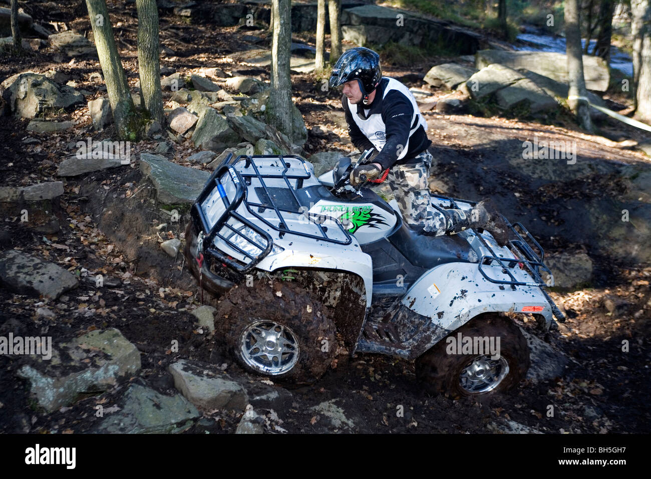 A young man in protective wear rides all terrain vehicle off road during 4 wheel trial competition. Stock Photo