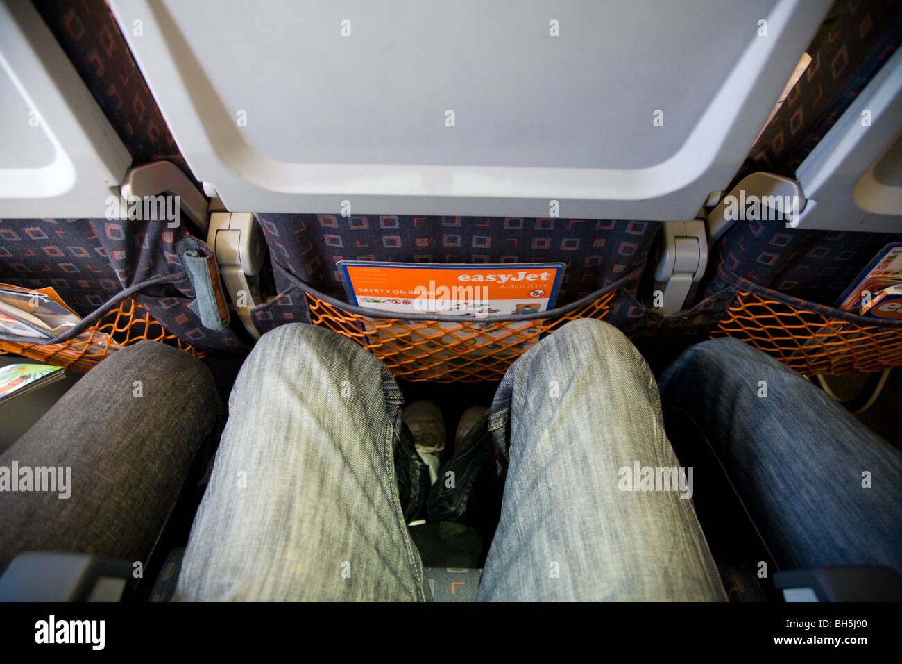 Passenger's legs wearing denim jeans shown while sitting in a plane