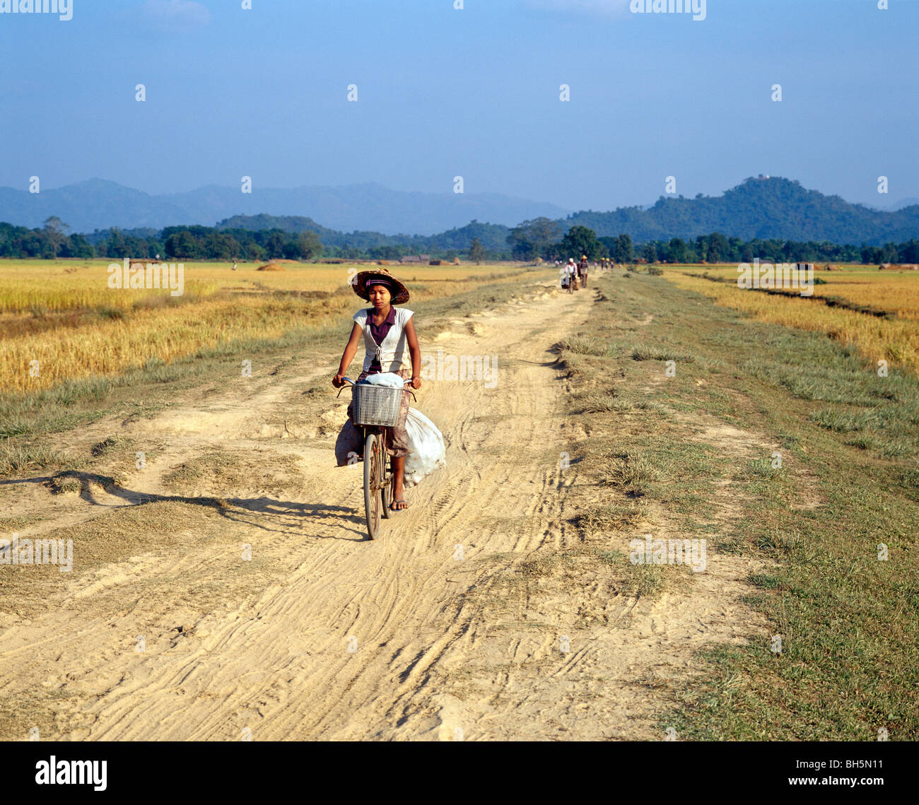 burmese girl cycling on a dusty farm track in the warm evening light Burmesische Radfahrerin auf staubigem Feldweg Myanmar Burma Stock Photo