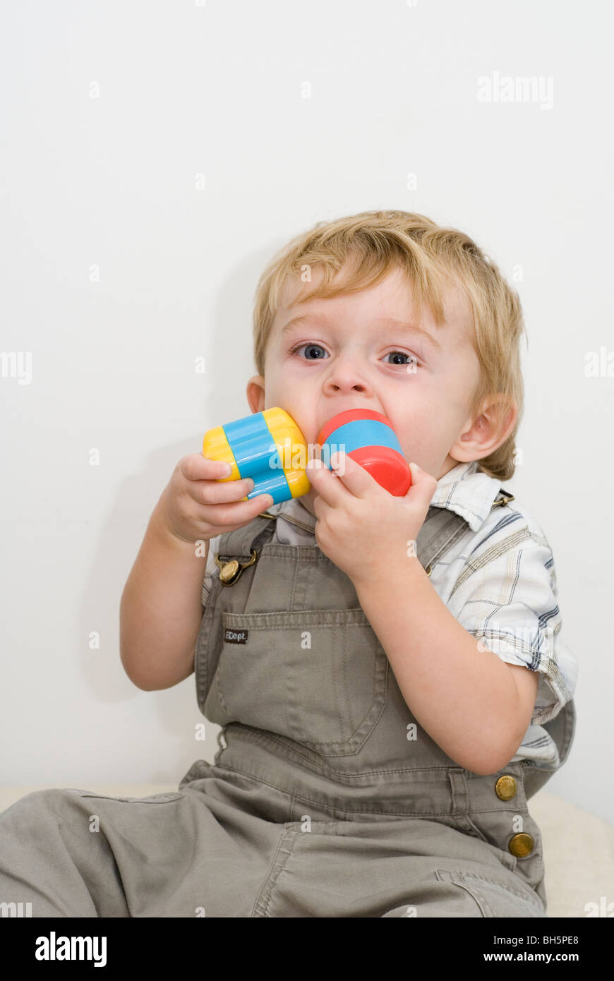Toddler Boy Aged 19 Months Stuffing Rattles from Shape Sorter Toy in Mouth, Isolated on White Stock Photo