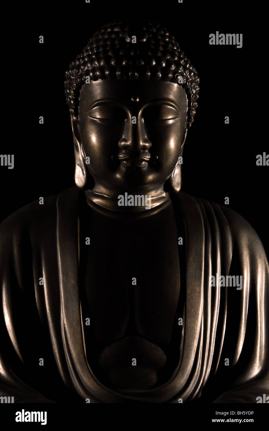 Bronze Buddha statue with a dark background and highlighted features Stock Photo