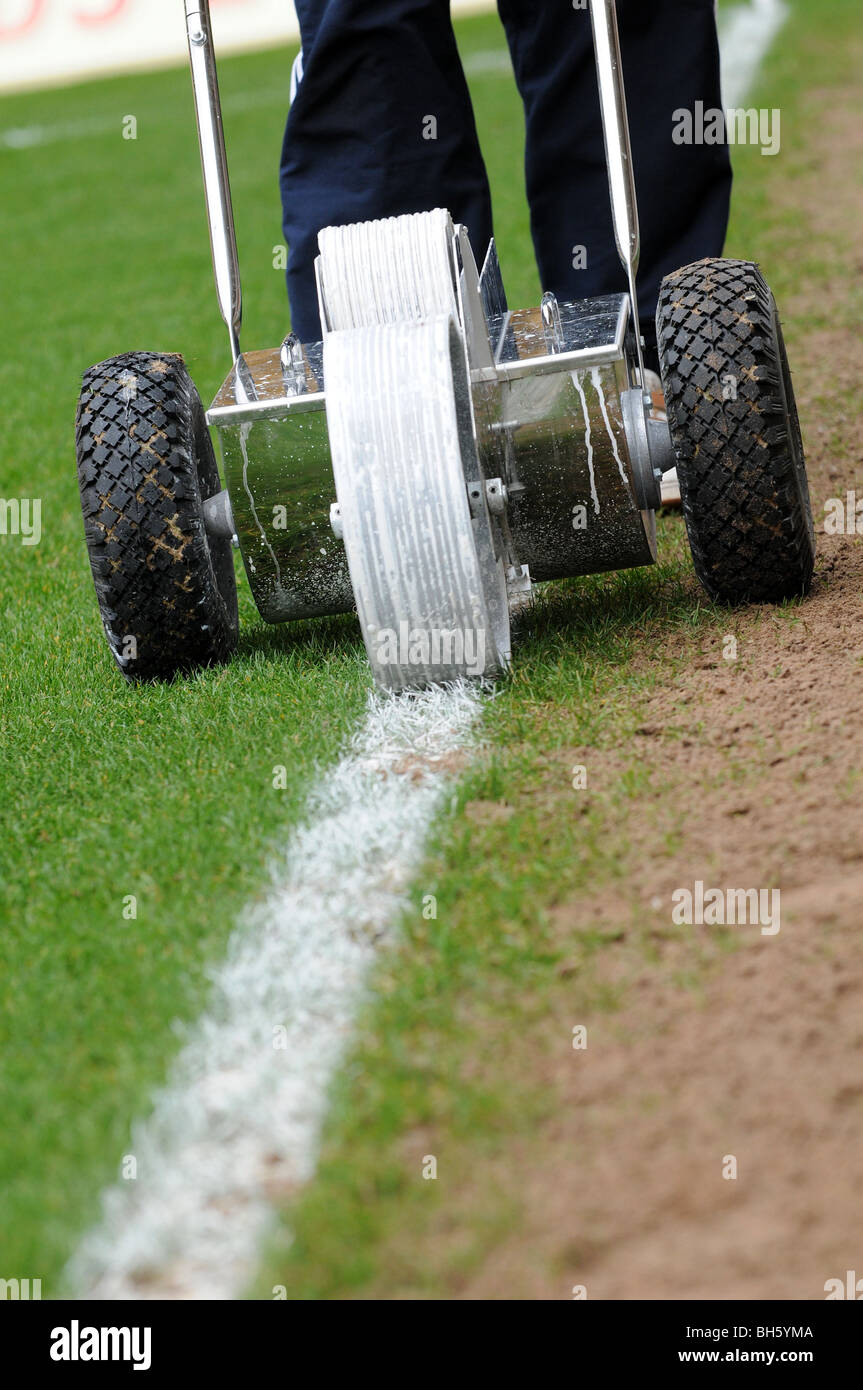 Groundsman putting a white line down a football pitch using a push-along machine to lay the paint on the grass, line marking Stock Photo