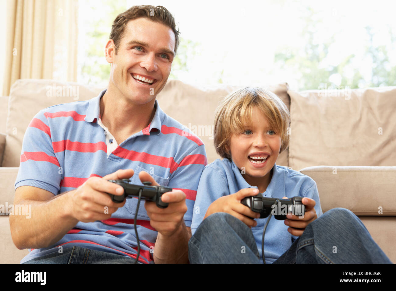 Father And Son Playing Computer Game On Sofa At Home Stock Photo
