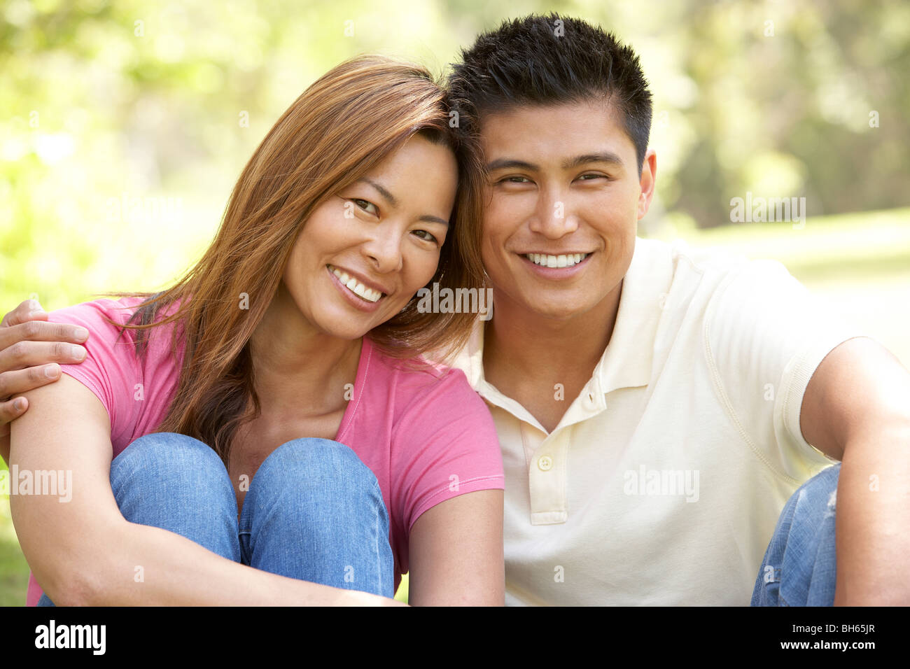 Portrait Of Young Couple Sitting In Park Stock Photo - Alamy