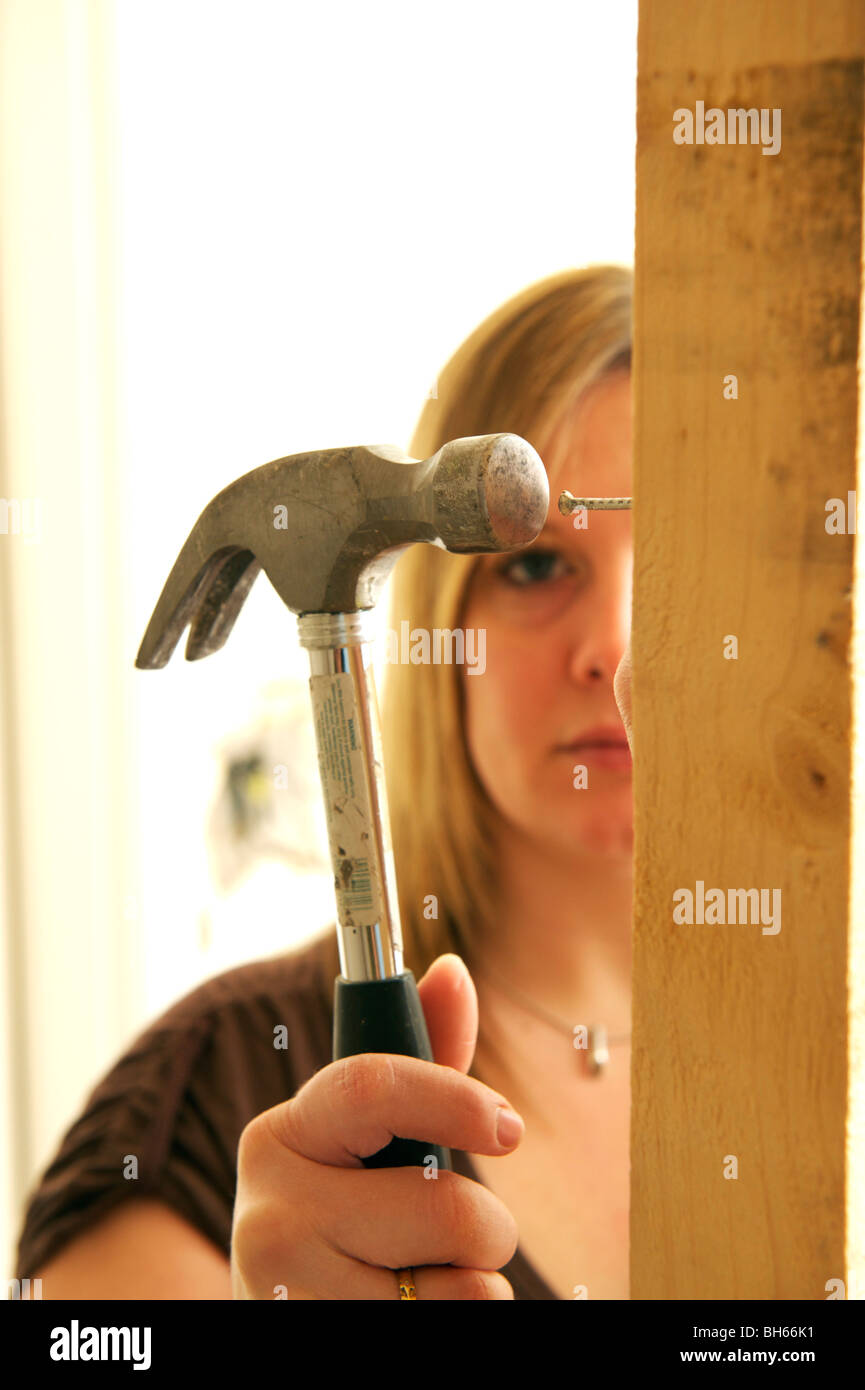 Young female hitting a nail with hammer during DIY project Stock Photo