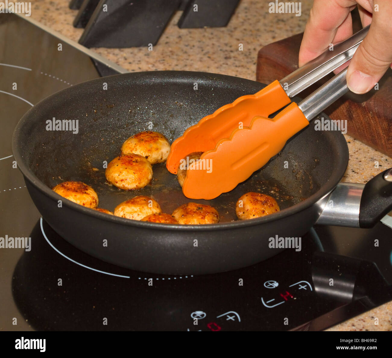 Sauteed fresh button mushrooms being served with tongs from the frying pan Stock Photo