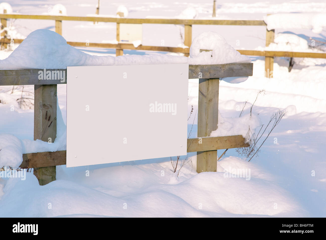 A blank white sign on a fence after recent snow fall, add your own message. Stock Photo