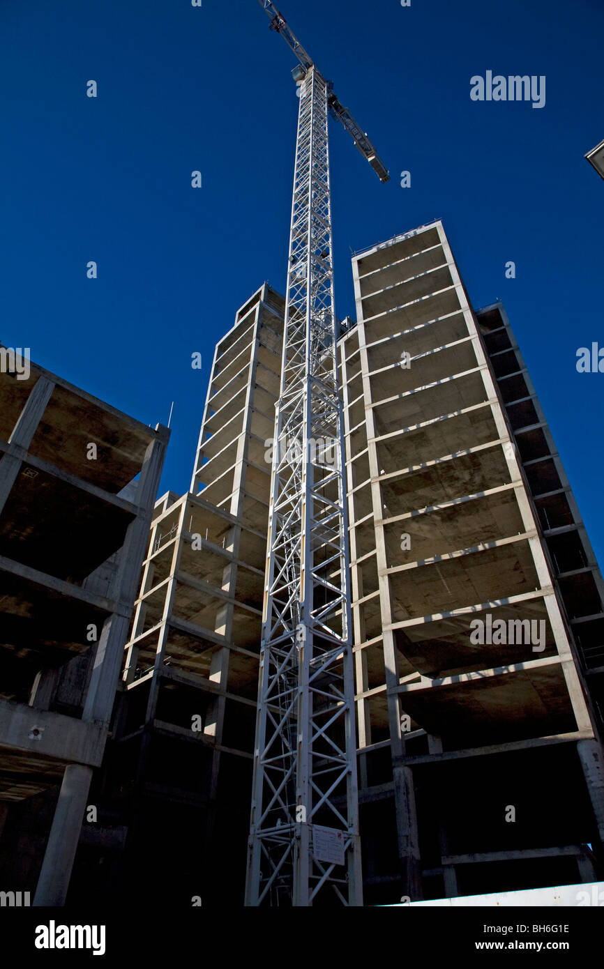 Crane stands by tall high rise building on construction site against blue sky Stock Photo