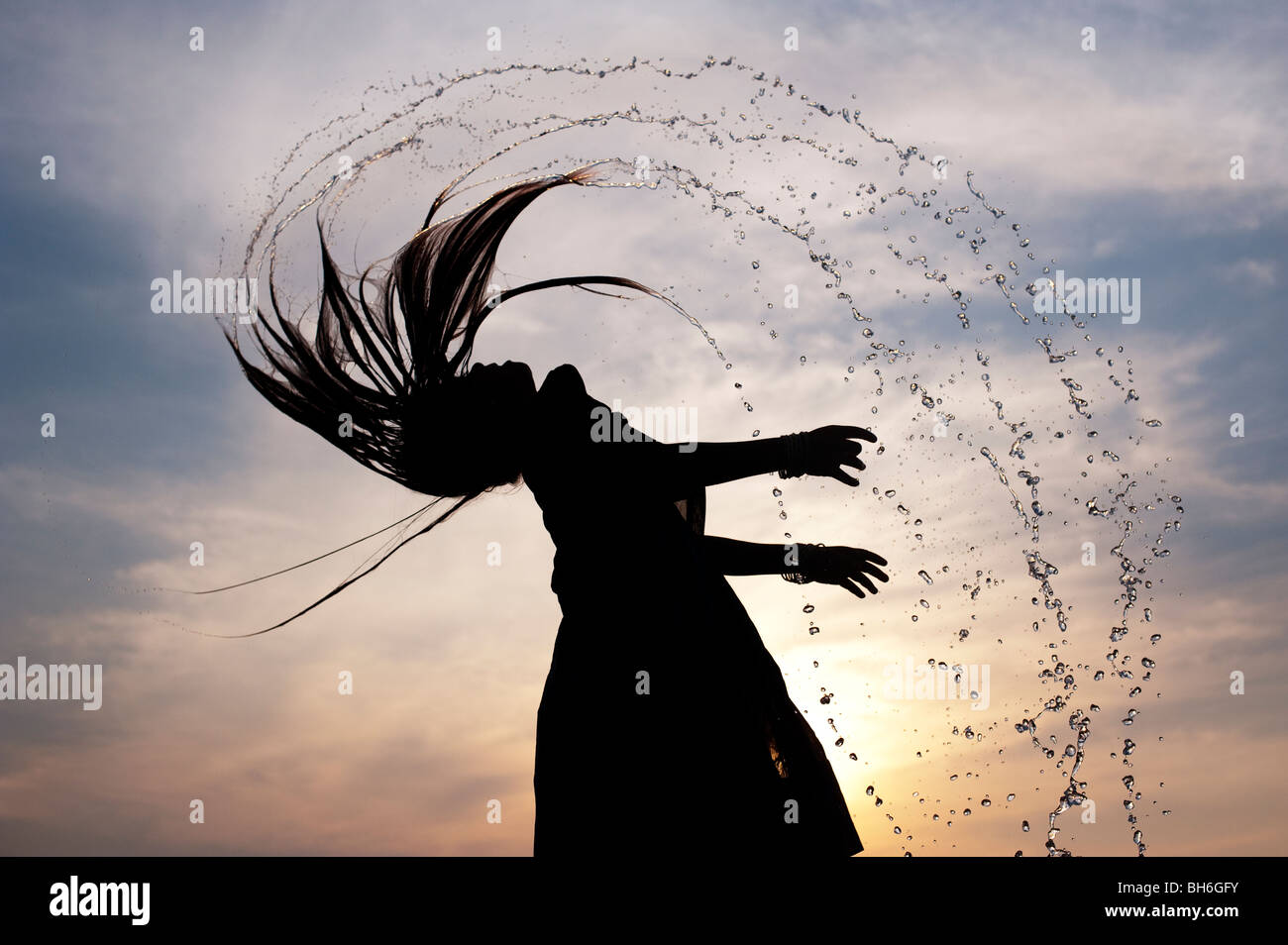 Indian girl throwing her wet hair back causing water spray silhouette. Andhra Pradesh, India