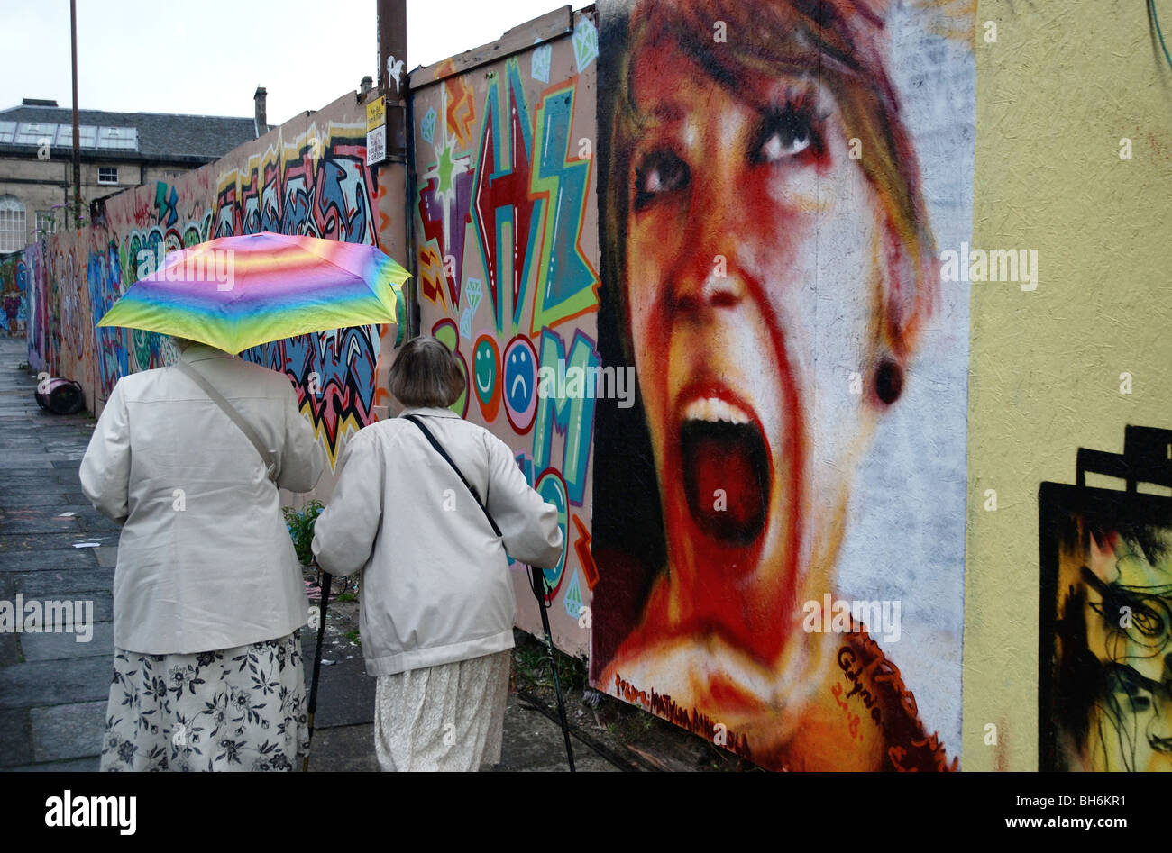 Two ladies walking in the rain past graffiti of a girl's head in Potterrow  Edinburgh Stock Photo
