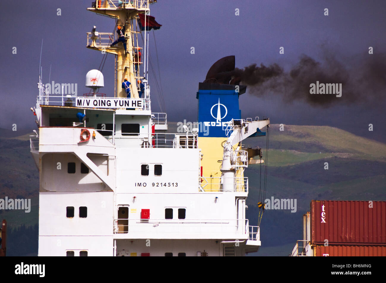 A container ship emits smoke from it's funnel while berthed at a container terminal Stock Photo
