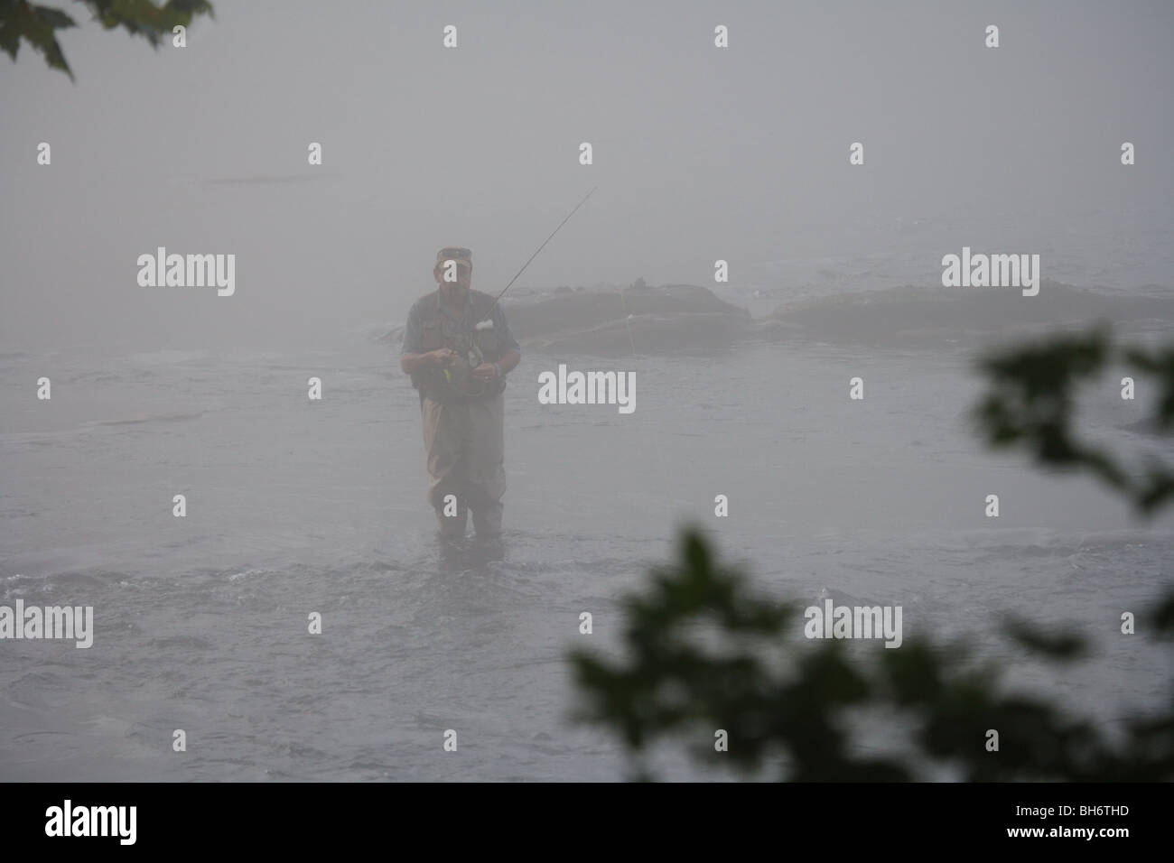FLY FISHERMAN FISHING IN RIVER CARRYING FLY ROD HEAVY FOG BAD WEATHER Stock Photo