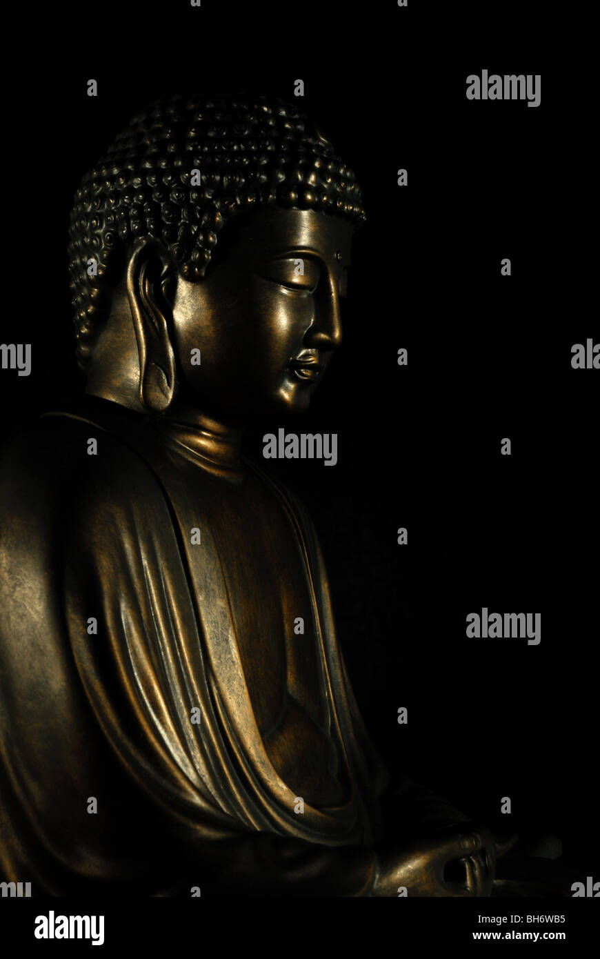 Bronze Buddha statue with a dark background and highlighted features Stock Photo