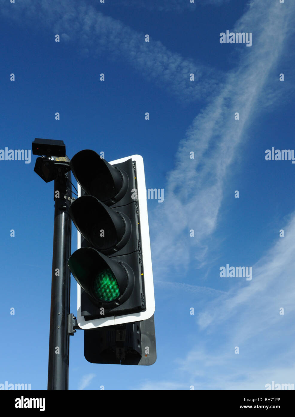 Traffic light set on green with dramatic blue sky with jet contrails behind Stock Photo