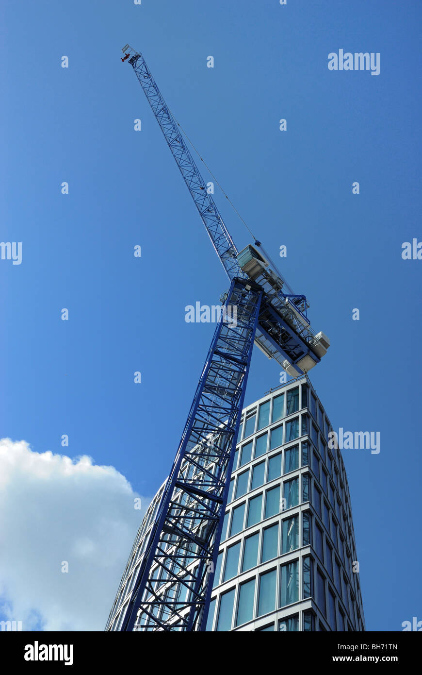 Construction crane in bright sunny weather with tall building  and a cloud behind Stock Photo