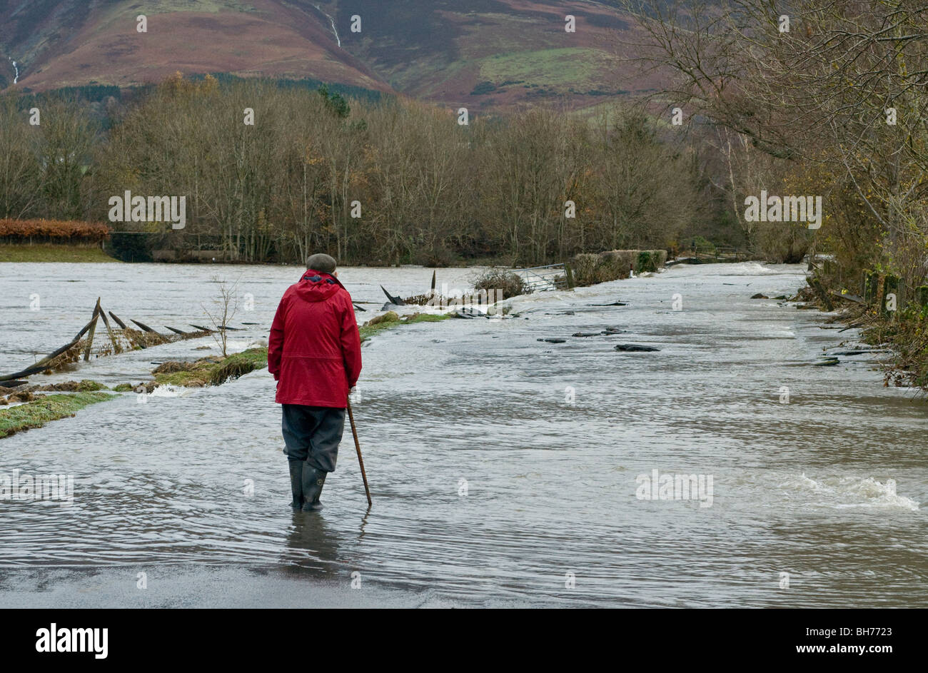 Solitary man in a red jacket wondering at the floodwater rushing past just outside Keswick in November 2009. Stock Photo