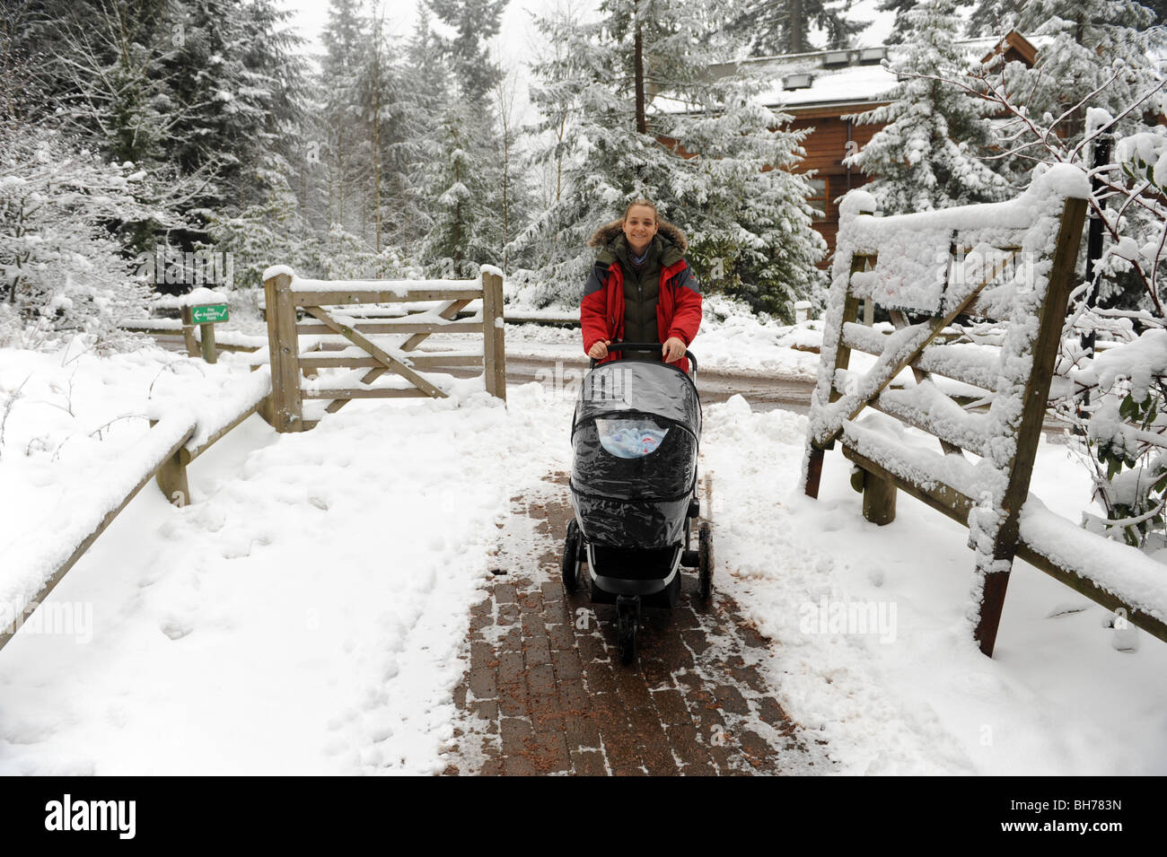 Young mother pushing baby buggy in winter wonderland of snow England Uk