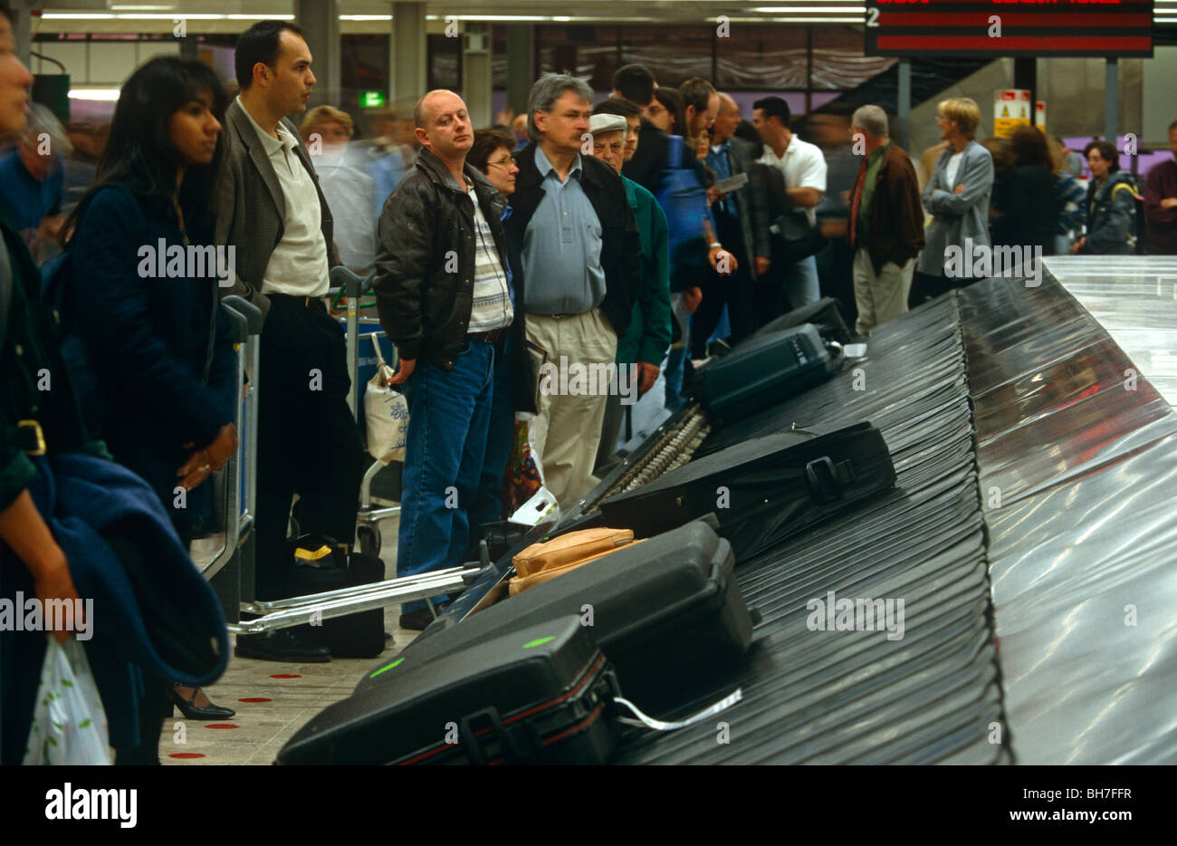 Arrival crowds wait for their baggage to arrive on a carousel during a busy holiday weekend at Glasgow airport. Stock Photo