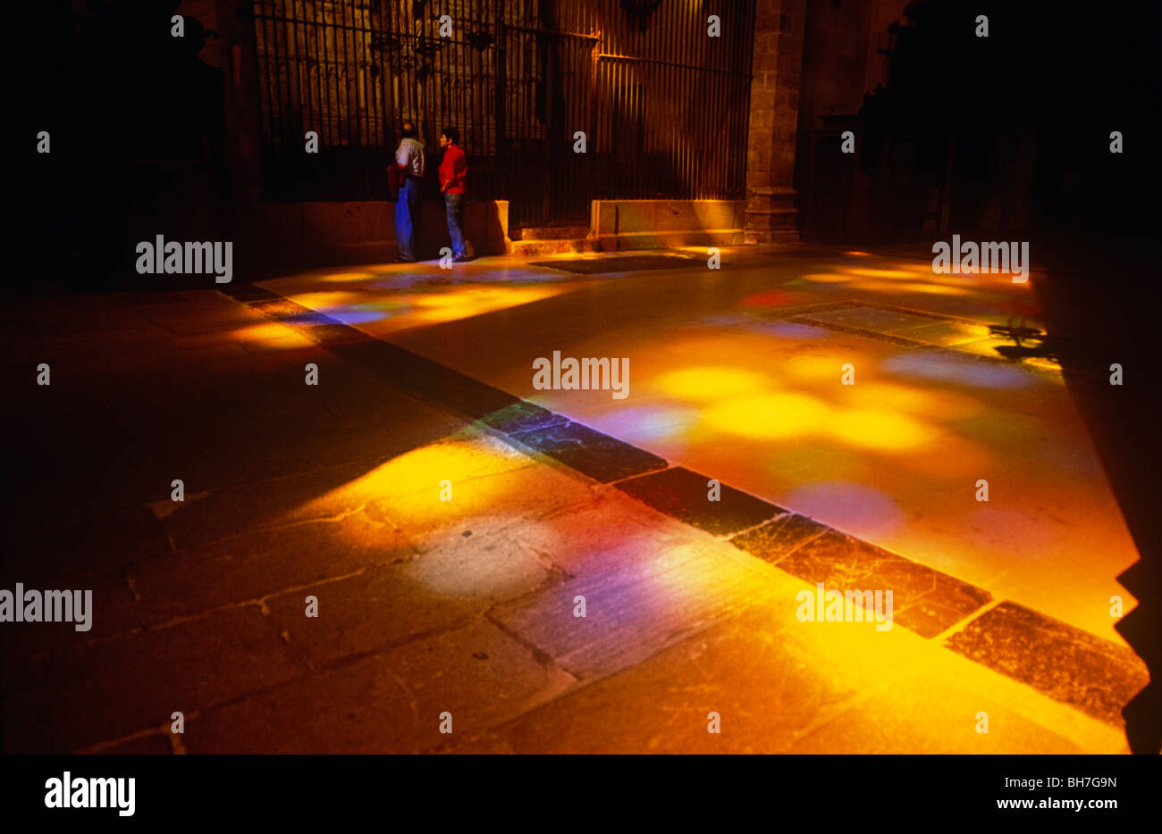 Stained glass light shines on to visitors and the floor of Palma's La Seu Cathedral in Mallorca. Stock Photo