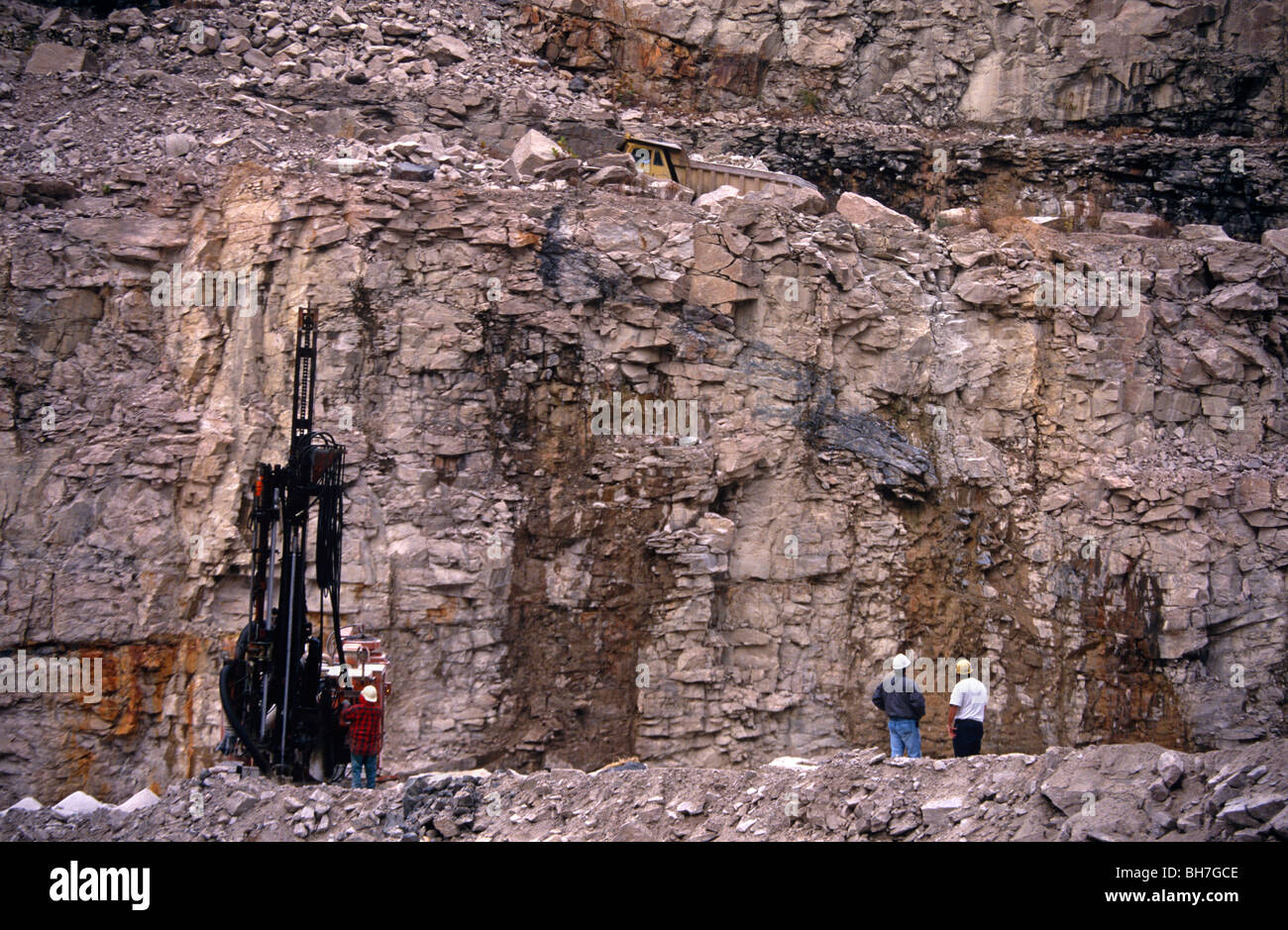 Three quarry workers and a boring drill machine are seen against rock strata in an open-air North Carolina pit. Stock Photo