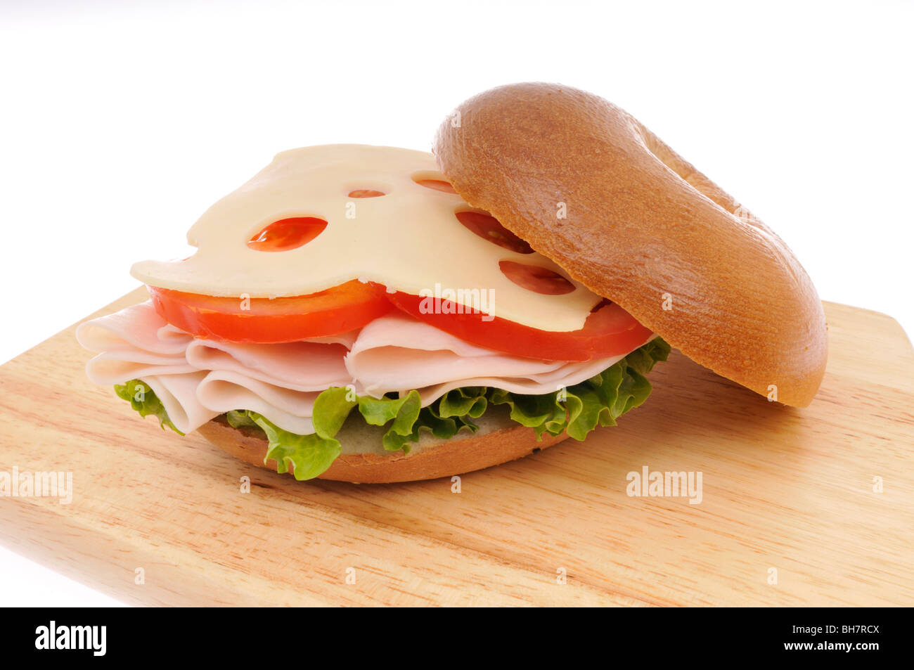 Open faced turkey, swiss cheese, lettuce and tomato bagel sandwich on a wood chopping board on a white background Stock Photo