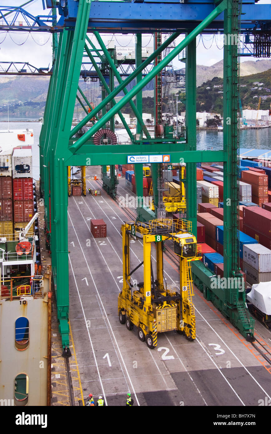 A straddle carrier at work underneath a container crane on the quayside at a container terminal. Seen from ship at terminal. Stock Photo