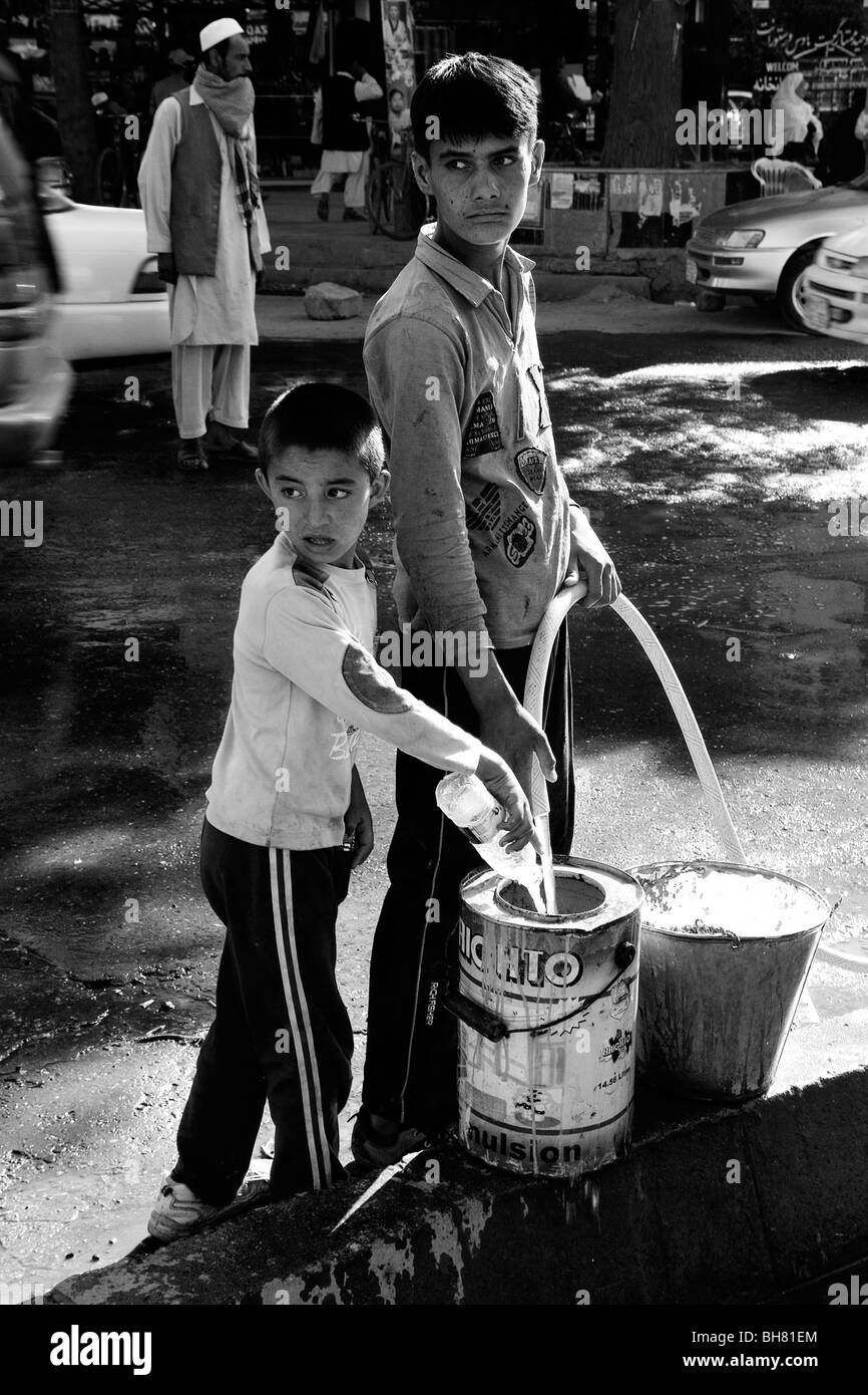 children filling water cans by roadside in Kabul Afghanistan Stock Photo