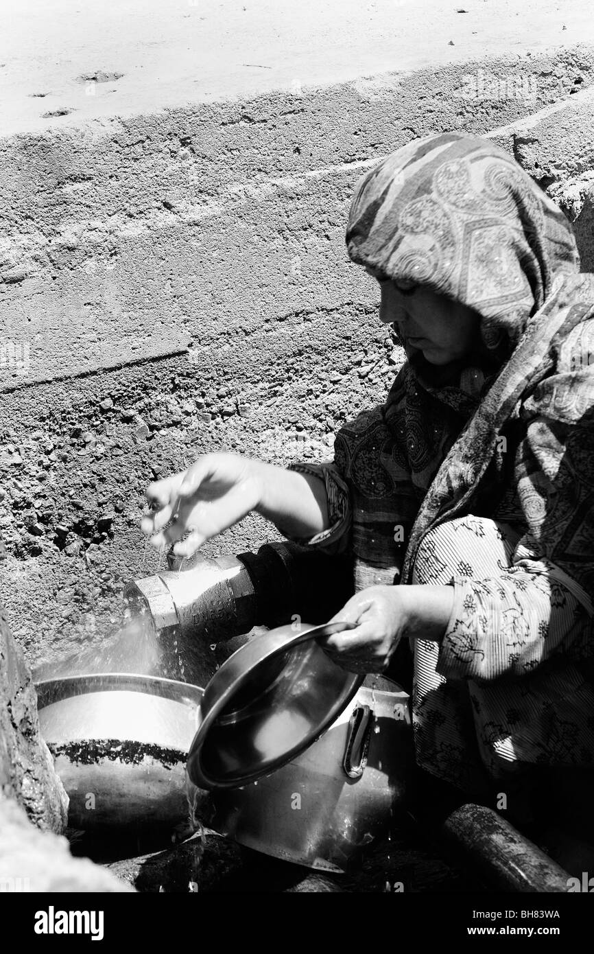 woman washing pots and pans in open hole with stand pipe in Kabul Afghanistan Stock Photo