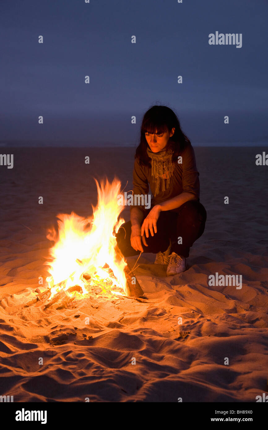 A woman staring into a fire burning on a beach Stock Photo