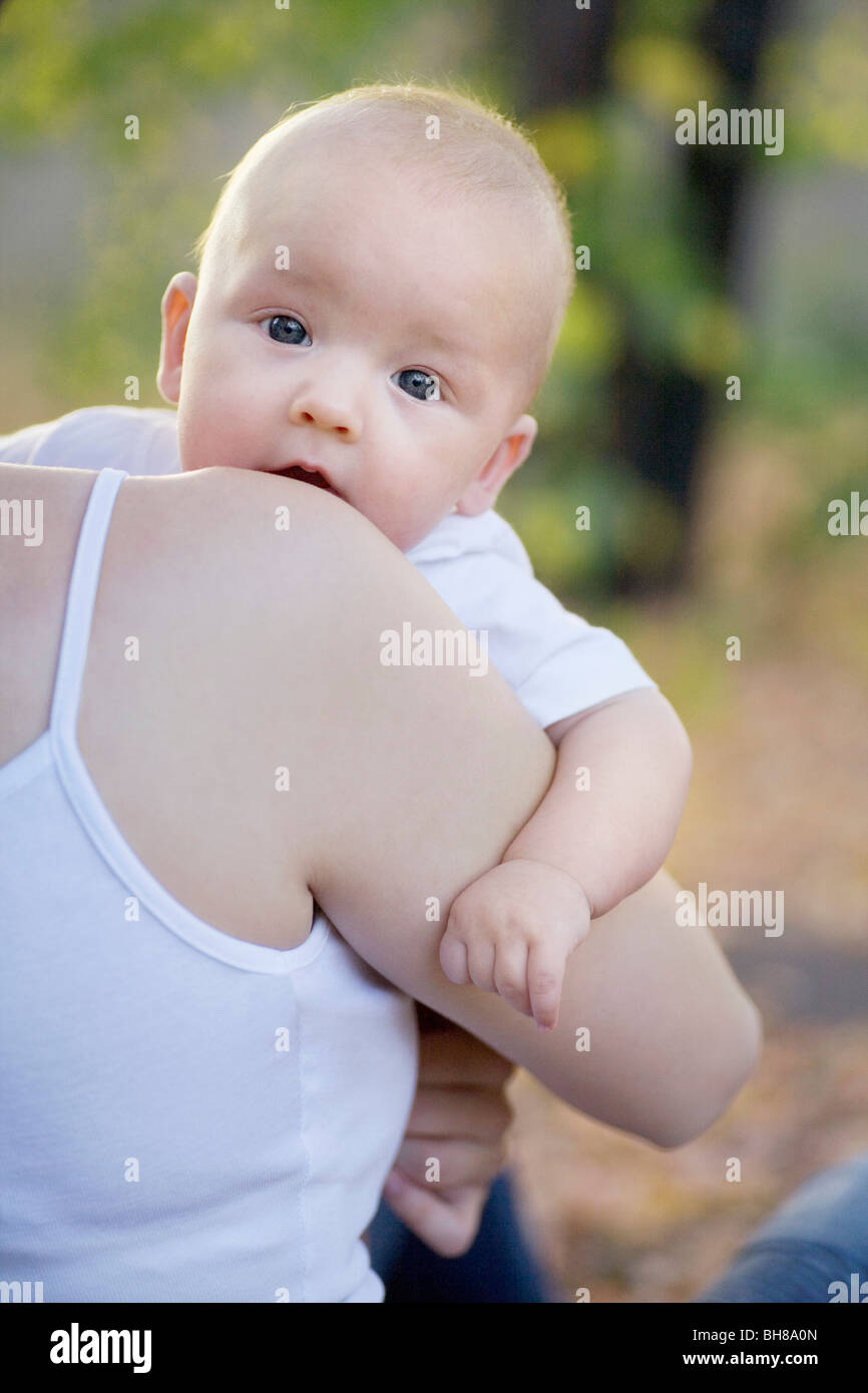 A baby boy being carried by his mother, over the shoulder view Stock